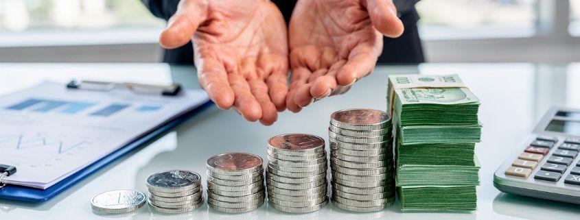 il-problema-delle-note-spese-tradizionali Uomo d'affari tiene in mano mazzetti di banconote e pile di monete.